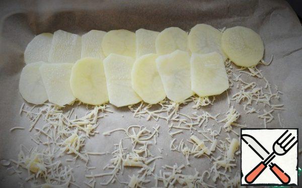 Grate half of the hard cheese on a fine grater, spread it on baking paper and place it in a baking tray (standard). Spread out the potato slices, overlapping.
Baking paper should be taken of good quality, so that it does not stick.
