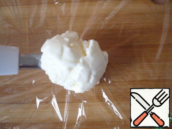 Now let's prepare Tartufo: prepare a sheet of food wrap on which you will be comfortable to collect the dessert. Using a large ice cream spoon, dial a ball of vanilla ice cream and leave it in the spoon.