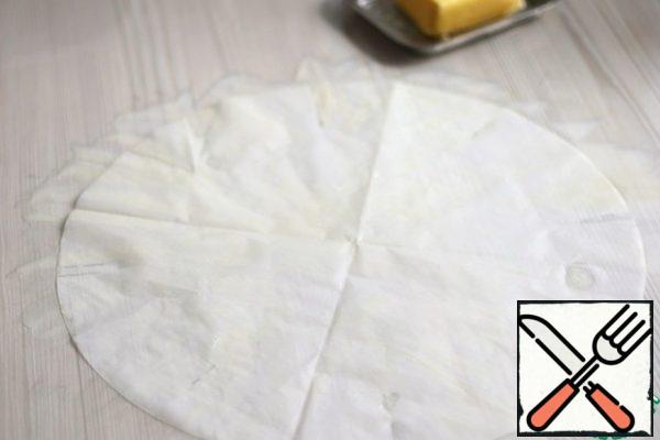 Before you begin to prepare the dough for the pie, a sheet of parchment of a round shape is smeared with a thin layer of butter. Repeat the procedure twice, i.e. grease two sheets of parchment with butter.