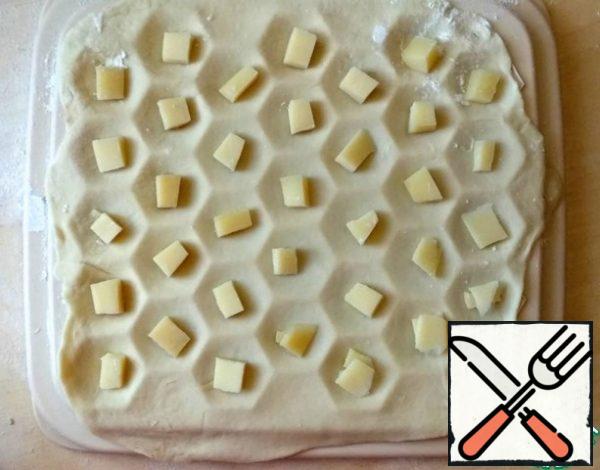 Knead the dough, cut off a piece, roll out into a layer and cover the form with it. Put the pieces of cheese in the cells.