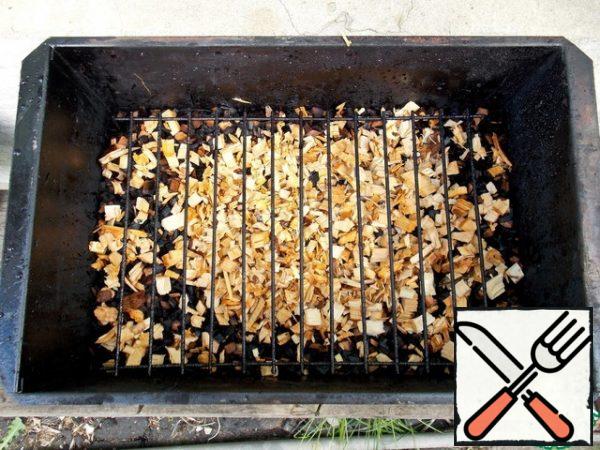 Moisten wood chips for smoking, not too much, with water and put them on the bottom of the smokehouse in an even layer one centimeter thick. Wood chips from alder, cherry or apple trees are best suited. In no case do not take coniferous chips, the fish will turn out to be bitter because of the resin in these rocks. Install the first grid. Place a baking tray to collect the fat and liquid.