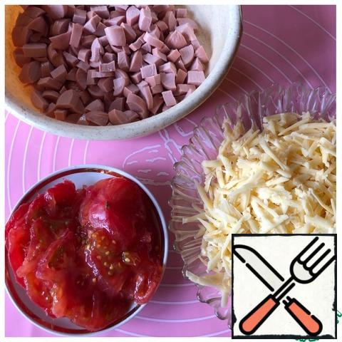 Prepare the filling. Peel the garlic, cut the sausages into small cubes, grate the cheese on a coarse grater, and cut the tomatoes into thin rings.