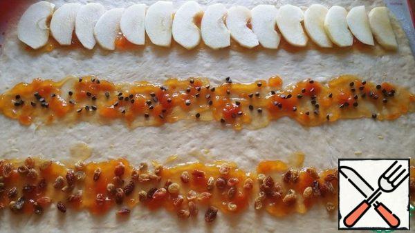 On the rolled out layer of dough, put in three rows of apricot jam 1-1. 5 full spoonfuls, retreating from the edges by 4-5 cm. On the first row we put apples, on the second nuts (I have a replacement for chocolate drops) on the third - soaked and pressed raisins.