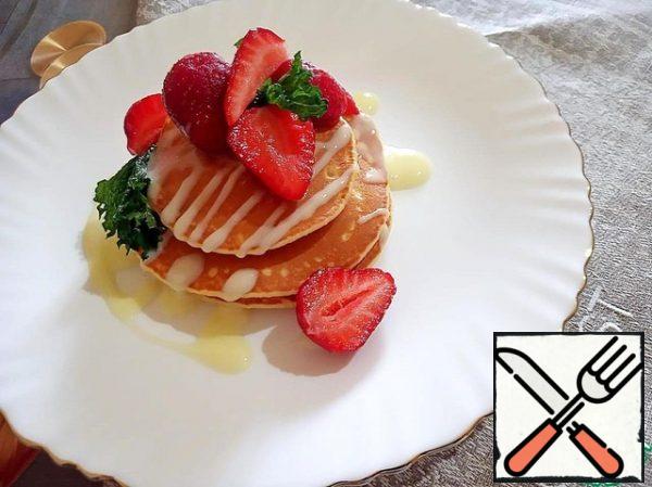 Ready-made pancake spread on a serving plate, pour condensed milk, decorate with strawberries and mint.