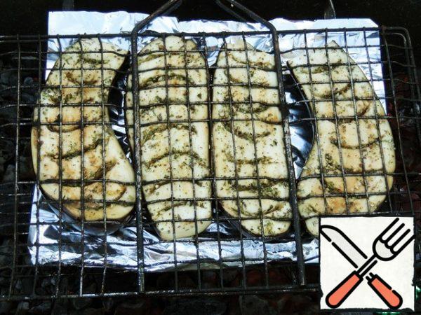 On the grid, put a sheet of foil, on it - eggplant halves skin to the foil. Fix the lid and fry on the coals for 10-15 minutes, turning.