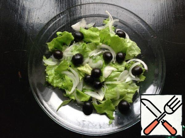 In a plate for serving lettuce, pick the lettuce leaves by hand.  Top with olives and onions, cut into thin half rings.