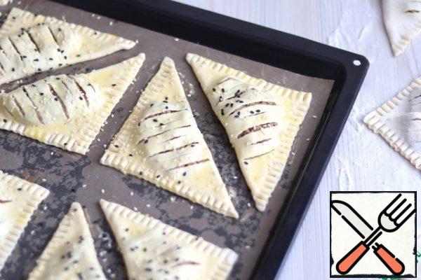 Place the triangles on a baking sheet covered with parchment or silicone Mat. Grease with beaten egg and sprinkle with sesame seeds. Send the baking sheet to a preheated oven to 190-200C. 