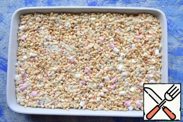 I grease a rectangular ceramic form with a small amount of butter and transfer the prepared mixture. I level it all over the surface and press it down on top. The dessert is sprinkled with confectionery sprinkles.
