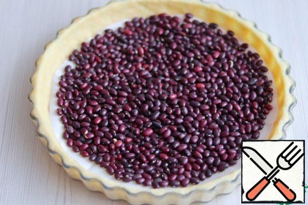 Cut a circle from a sheet of parchment, place it on a layer of dough, then pour a layer of beans or peas. This must be done in order to prevent further bubbles from forming on the surface.