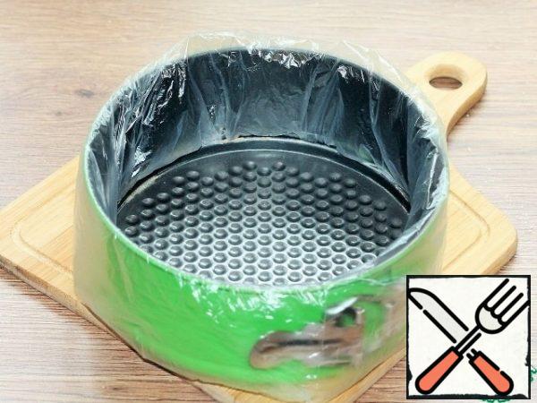 Prepare a split form f=18 cm for baking. Remove the bottom and put a transparent bag. Return the bottom of the mold to its place and cover with baking paper.