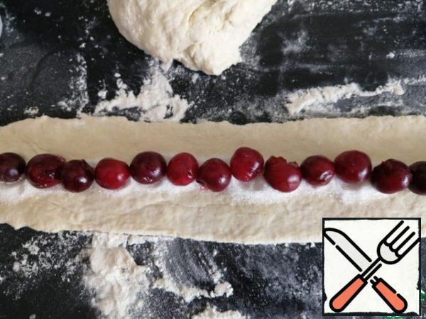 Knead the elastic dough, add flour if necessary, roll out the dough, cut into strips 30 cm long and 8 cm wide. Put the sugar in the center and the cherries, peeled from the seeds, on top.