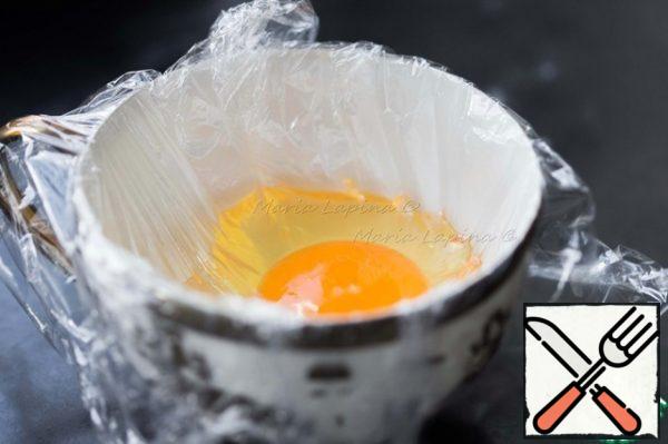Put food wrap in a Cup, grease with vegetable oil and break an egg into it. Lift the edges and tie them. Try to keep less air in the film.