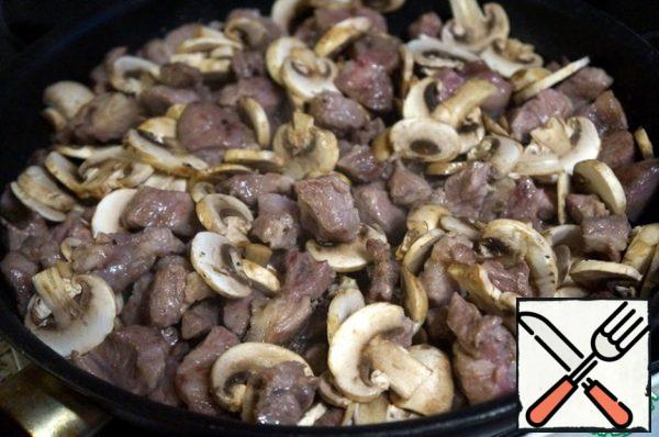 Put the mushrooms to the meat. Fry, stirring, until the mushrooms are ready.