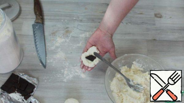 The dough is ready. Now we form cheesecakes. To do this, take a small part of the dough in your hands, add a piece of chocolate inside, cover the top with the dough and form a cheesecake with your hands.