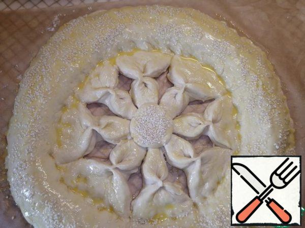 Each cut triangle is pinched in the middle. You should get a "flower". Grease the entire pie with yolk. Sprinkle the middle and edge of the cake with sesame seeds.