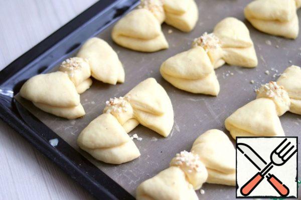 Put the formed buns-bows on a silicone baking Mat or parchment and put on a proofing (10-15 min.). then grease with beaten egg. Sprinkle the middle with fried and crushed almonds. Send the rolls to the oven preheated to 190C and bake until Golden.