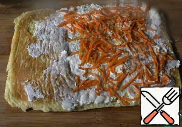 Grease the cooled layer with cream of curd cheese with sour cream, not reaching the edge. Put the carrots on top in Korean.