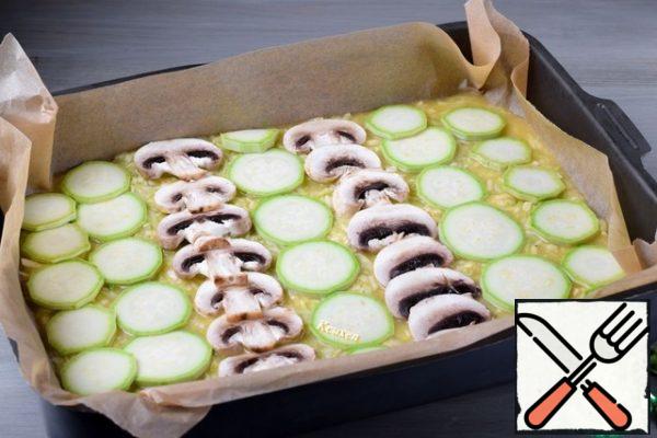 Preheat the oven to 200-205°C. Cover the baking sheet (approximate size 25 X 35 cm) with baking parchment and put the zucchini mass. Level it out. Half of the zucchini cut into thin circles, mushrooms-thin slices. Arrange the pieces of zucchini and mushrooms on the surface of the zucchini mass in any order.
