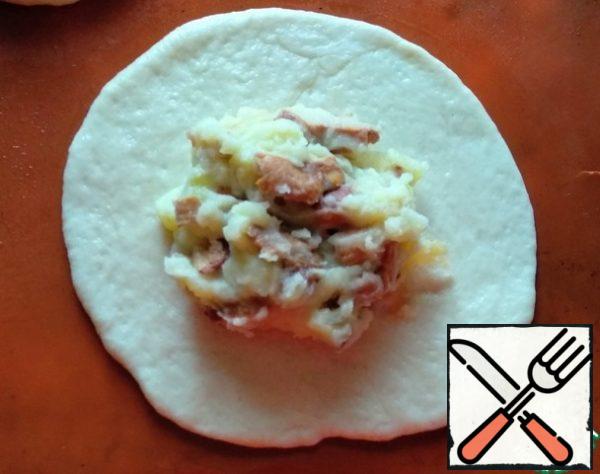 Next, knead the risen dough and divide it into 12 parts. The pies will turn out quite large, so you can optionally divide them into more parts. Roll out each part in a circle, approximately 5-6 mm thick. In the center, put the filling 1-1.5 tbsp.