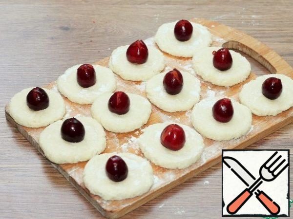 On a surface dusted with flour, spread out the balls and press with your hand or glass. You should get a round tortilla.Put one berry in the middle of the tortilla. Wrap the edges of the dough up, carefully closing the berries.