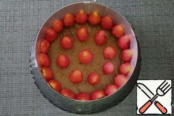 Ready to cool the sponge cake and put it in a split ring, the sides of which are previously lined with film. On the sponge cake in a circle, put the strawberry halves cut to the sides of the form, and in the middle - whole berries.