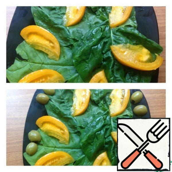 Spinach leaves are washed and dried. We put it on a plate. Cut the tomato into thin pieces and send it to the spinach leaves. Cut the olives in half and put them on a plate.