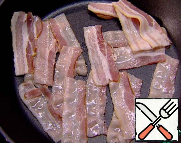 In a preheated frying pan, fry the bacon slices.