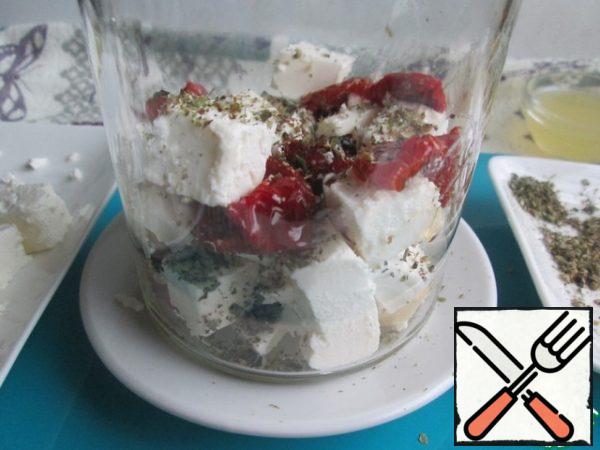 In a dry jar, lay out layers of cheese, dried tomatoes and dried herbs. Leave a pinch of herbs to add to the oil.
