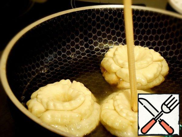 Preheat vegetable oil (or a mixture of vegetable and ghee) in a deep frying pan or saucepan.
For the test, lower a small piece into the oil, if it is hot enough - the edges of the dough will begin to bubble and blush.
Now you can bake crumpets on medium heat. With a thin stick, pierce the center of the "pyramid", lower it into the oil and rotate it quickly around the axis. The oil will penetrate between the layers and the crumpets will begin to "bloom". Thanks to the hole in the dough from the stick, the oil boils in the center of the crumpets, and they are well baked, despite the layers.