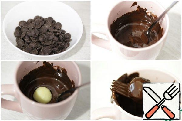 While the candy is cooling, melt the dark chocolate in the microwave or in a water bath. It is best to melt it in a small narrow container, so it will be more convenient to work with it.
Let the melted chocolate stand for about a couple of minutes, then remove the truffles from the refrigerator, dip each one in the chocolate and place on baking paper.