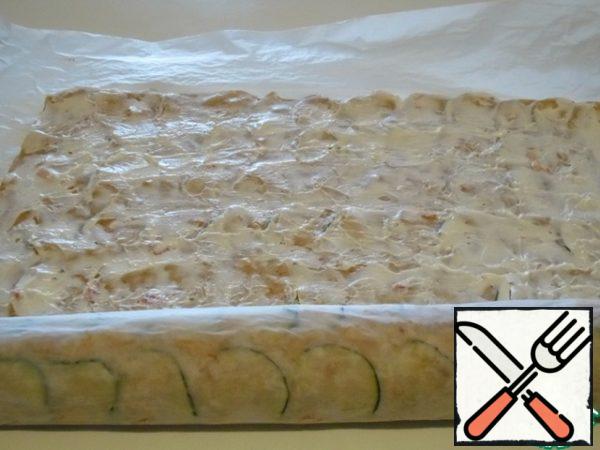 Using paper, make the first turn of the cake around the cheese, seal it and wrap it.