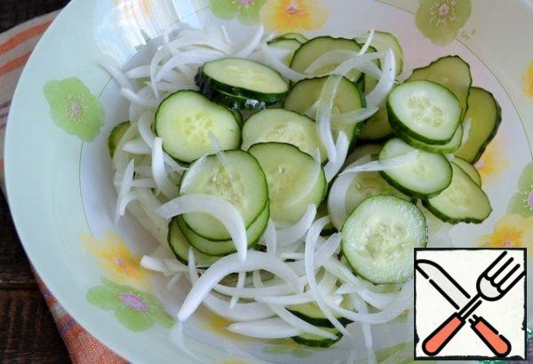 Peel the onion, cut it into feathers, and add it to the cucumbers.