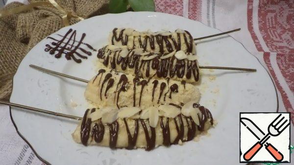 Break the chocolate, melt it in a water bath and decorate the bananas with it. Sprinkle the top with almond petals.
Freeze on a silicone Mat or plastic wrap, turn over, smear with honey and sprinkle with cookie crumbs, decorate to your taste and transfer to a plate!
 Bon appetit!