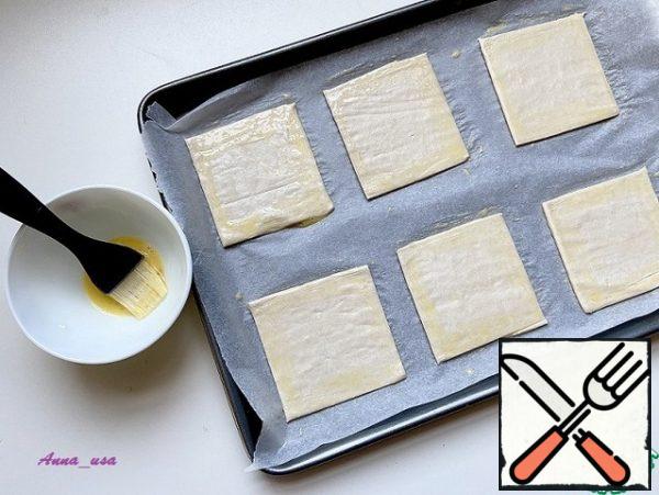 Cut the puff pastry into squares of about 9x9 cm. Cover the baking sheet with parchment and put the dough on it. Brush the edges of each square with the second half of the egg.