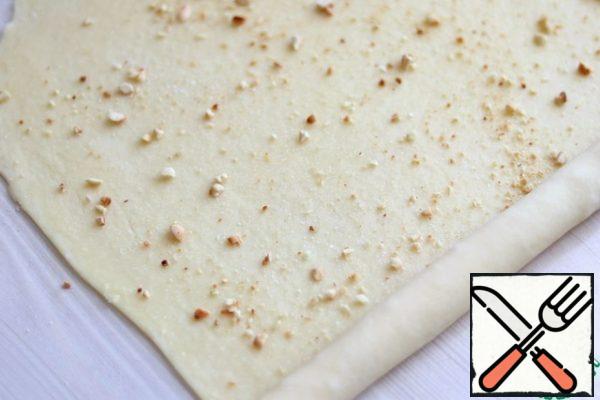 Next, roll out the dough into a thin layer about 3 mm thick, lightly lubricate!! melted butter, sprinkle with sugar and fried / crushed hazelnuts, roll into a roll. Pinch the seam.