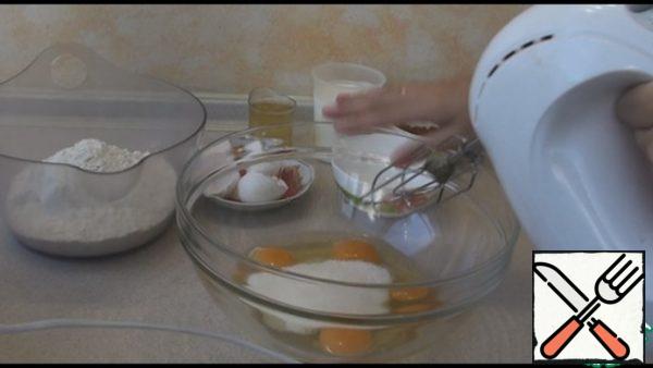 Drive the eggs into a deep container, add a pinch of salt, sugar, vanilla sugar and beat with a mixer so that the eggs brighten and increase in volume.