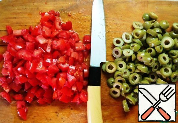 Cut tomatoes into small pieces and olives into rings.