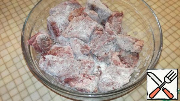 Pour the meat into a bowl, sprinkle with flour and mix well so that each piece is rolled in flour.