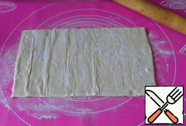 Let the puff pastry thaw, put it on a flour-dusted Mat. Cut the dough into convenient layers, roll it out slightly in one direction.
