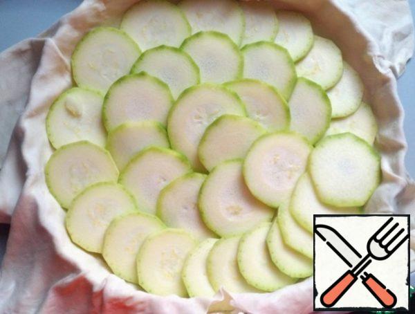 Wash the zucchini, peel it, and cut it into small circles. Spread out in the form.