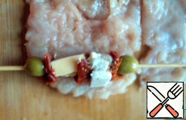 String olives, cheese, cheese and dried tomatoes on a skewer.