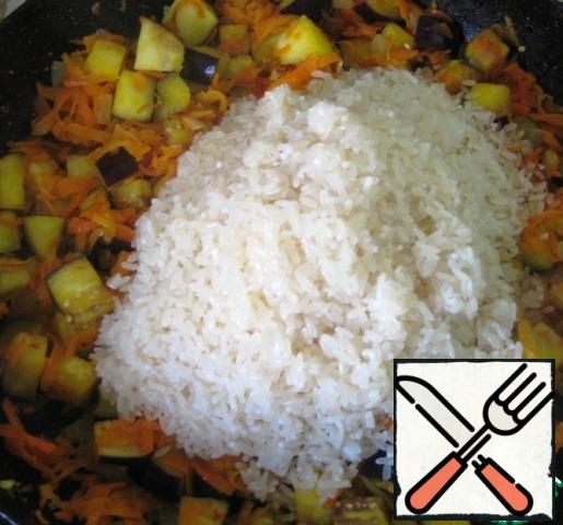 As soon as the eggplant changes color and becomes slightly soft, add the well-washed rice, removing the water as much as possible.
Mix thoroughly. Continue to fry the rice and vegetables, stirring every 2-3 minutes. Rice should become dry, amber.