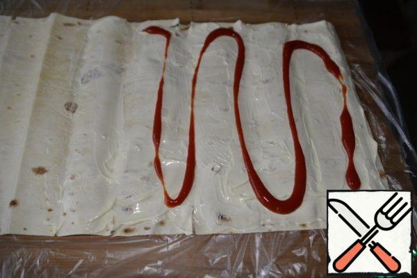 Spread the pita bread (roll) with a thin layer of mayonnaise, make strips of ketchup on top.