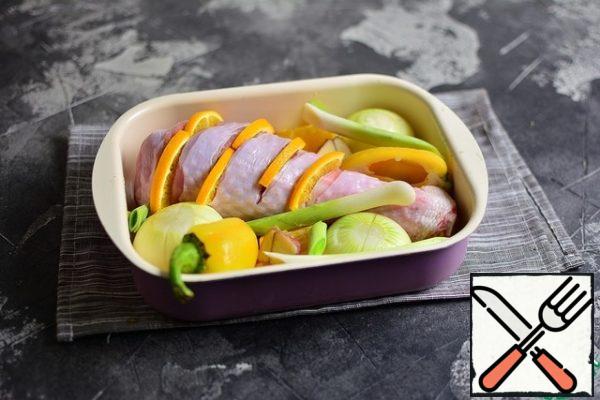 Put the drumstick in a baking dish, then put the pepper cut in half, onion, cut crosswise on top, garlic cloves and leeks to taste. The remaining orange is also put in the form.