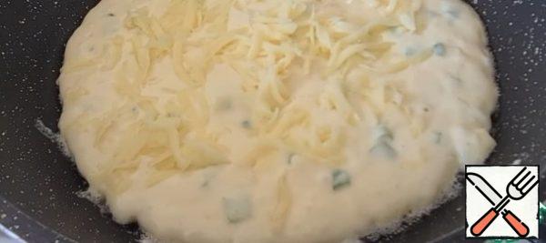 Preheat the pan, I have a diameter of 24 cm, grease with oil, put part of the dough, flatten, sprinkle with grated cheese
