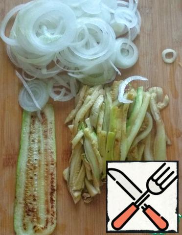 Peel the onion, wash it, and cut it into thin half-rings. Cut the zucchini into strips.