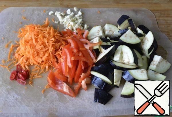 Vegetables are washed, cleaned, and cut. Eggplant cut into cubes or half rings. Pepper cut into strips. Hot pepper rings. Garlic is also crushed. Three carrots on a grater.