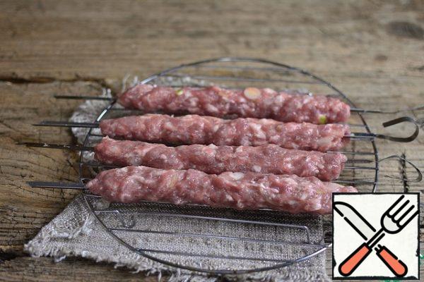 Often wetting your hands in cold water, distribute the minced meat on skewers with a thick sausage.