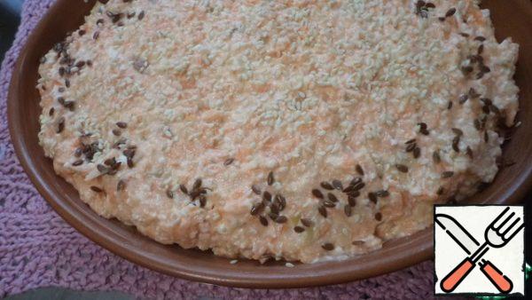 The baking dish is greased with oil and filled in. Sprinkle sesame seeds on top and flax on the edges.