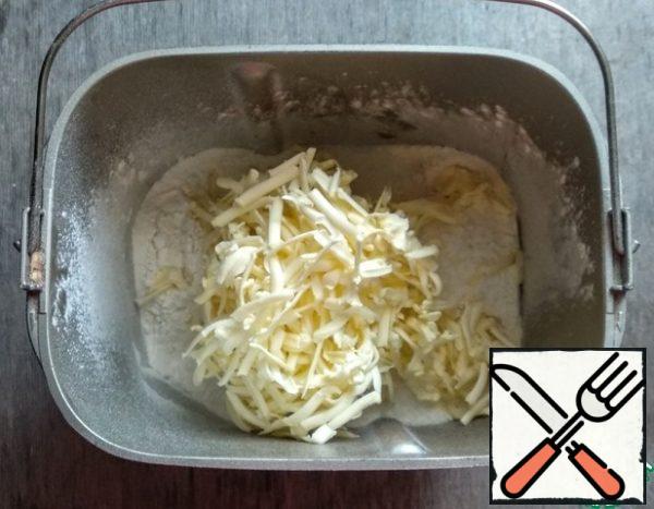 I will knead the dough in a bread maker. Sift the flour, add salt and sugar to the bread maker bucket. Grate the butter on a coarse grater.